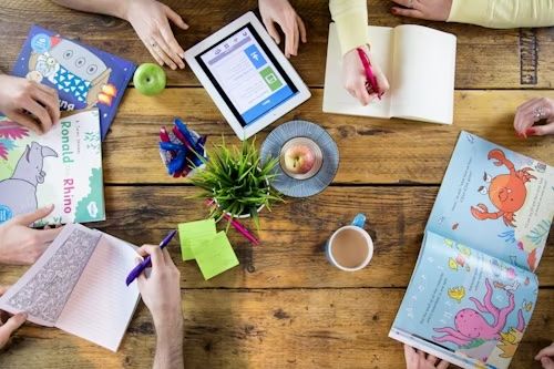 Kinderhände mit Büchern, Tablet und Bastelmaterial auf einem Holztisch